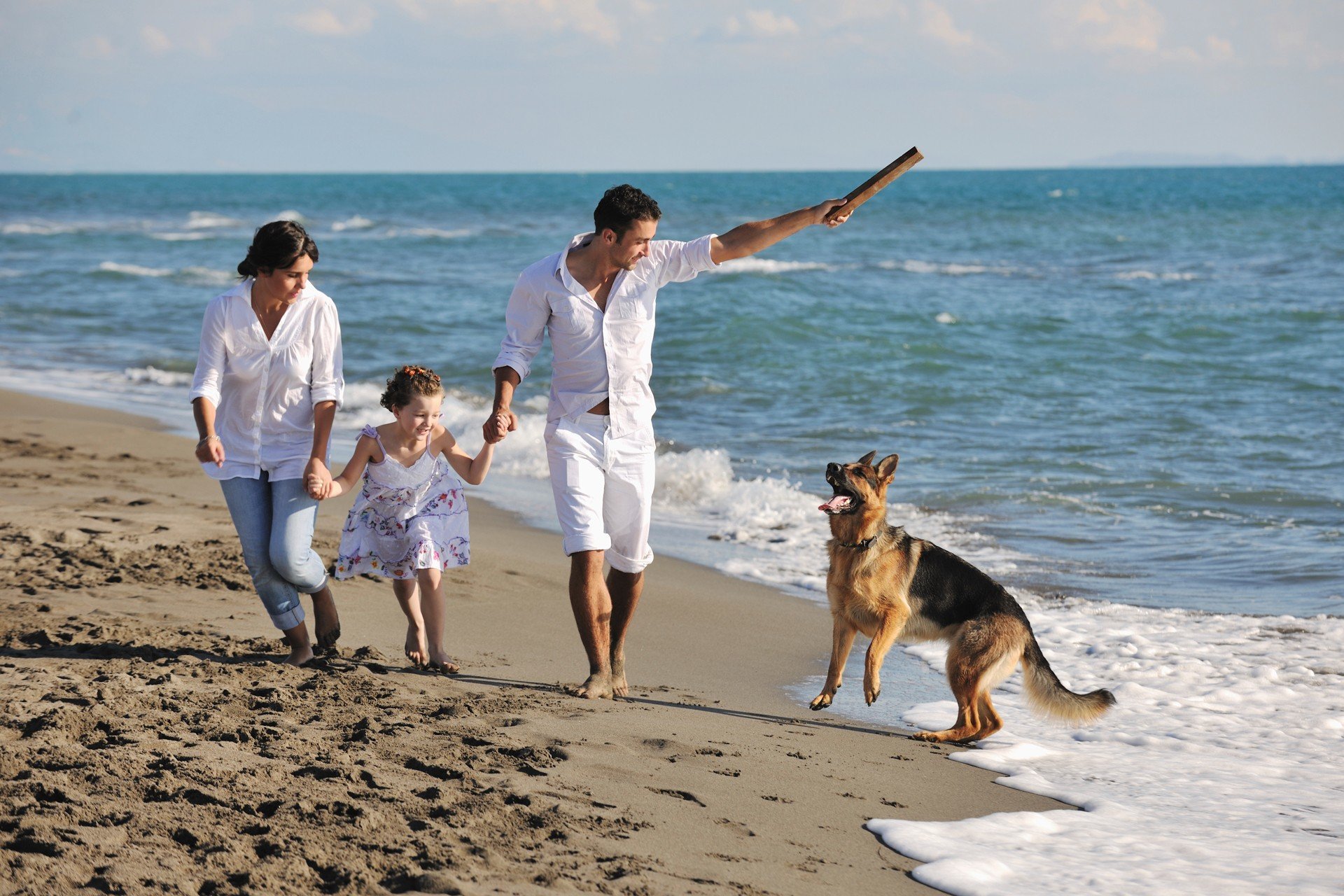 Glückliche Familie mit Hund am Strand spielen