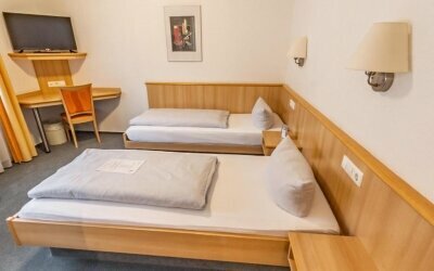 Die Zimmer sind klassisch und gemütlich eingerichtet, was den traditionellen Charakter des Hotels unterstreicht. Die Möbel sind aus Holz gefertigt, was eine warme und einladende Atmosphäre schafft. Die warme Farbgestaltung des Zimmers trägt zusätzlich zur