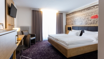 Moderne, helles Hotelzimmer mit Doppelbetten, teilweise Balkon und mit allem, was heutzutage zu einem pfiffigen Hotelzimmer dazu gehört. Wohnliche Materialien und aktuelle Farbkombinationen mit flottem Design. Einfach zum Wohlfühlen. Badezimmer mit Fenste