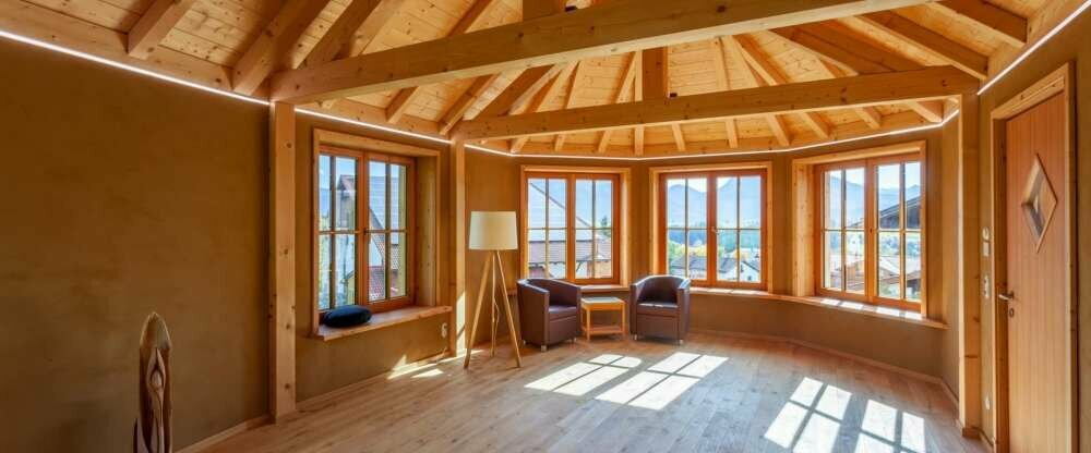 Raum am Bach mit hohem Holzgiebel, Lehm-Wandheizung, Holzboden und freiem Blick in die Natur; ideal für Entspannungs-Übungen und Meditation