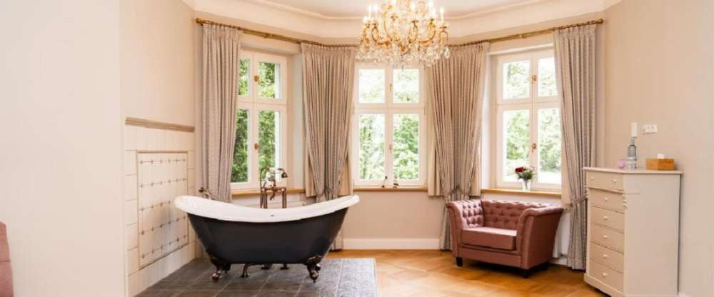 Diese Suite beeindruckt mit einer freistehenden Badewanne im Wohnbereich, gekrönt von einem stilvollen Kronleuchter. Chaiselongue, Sessel mit Fußhocker sowie ein großzügiger Eingangs- und Ankleidebereich schaffen ein luxuriöses Wohngefühl. 