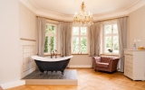 Diese Suite beeindruckt mit einer freistehenden Badewanne im Wohnbereich, gekrönt von einem stilvollen Kronleuchter. Chaiselongue, Sessel mit Fußhocker sowie ein großzügiger Eingangs- und Ankleidebereich schaffen ein luxuriöses Wohngefühl. 