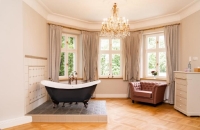 Diese Suite beeindruckt mit einer freistehenden Badewanne im Wohnbereich, gekrönt von einem stilvollen Kronleuchter. Chaiselongue, Sessel mit Fußhocker sowie ein großzügiger Eingangs- und Ankleidebereich schaffen ein luxuriöses Wohngefühl. 