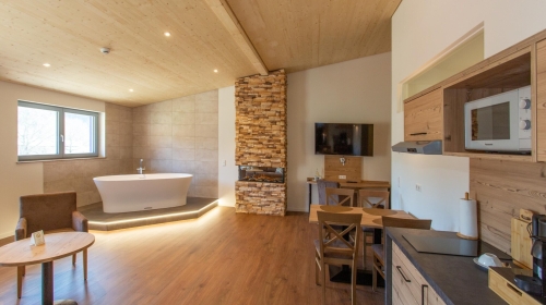 Moderne Suite mit Blick auf den Wald, Venylboden, freistehende Whirl- Badewanne und Show- Kamin im Wohnbereich, getrenntes Schlafzimmer, Sofa, Schreibtisch, Kitchenette, TV, Safe, Du/WC und Balkon (über den Lift zu erreichen)
